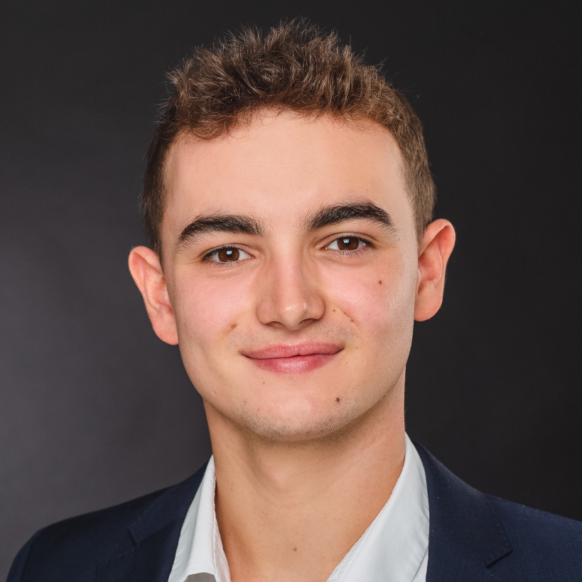 Leonard Arens trägt einen dunklen Anzug und ein weißes Hemd vor einem dunklen Hintergrund